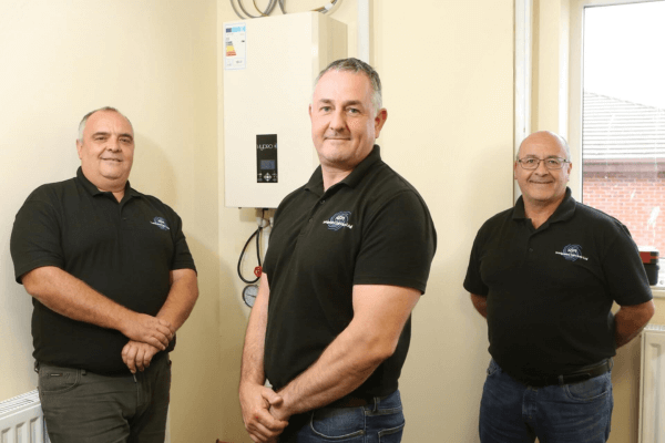 The three company directors from ASH Integrated Services in black shirts standing in front of a water heater