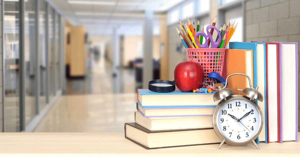 a stack of books, an alarm clock and other school supplies sit on a table