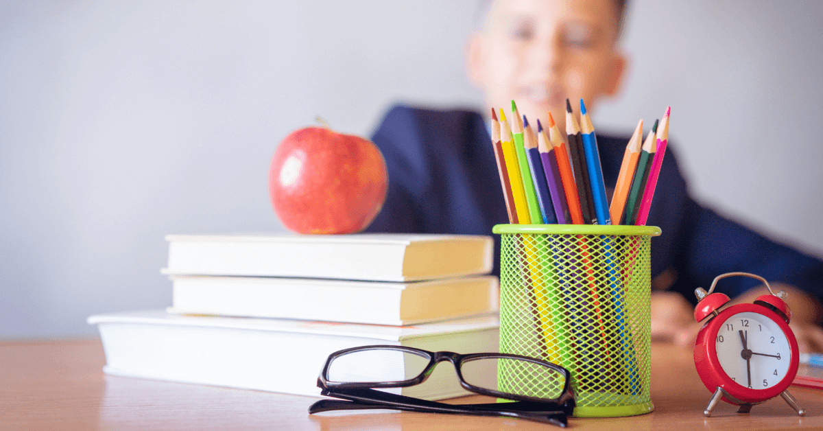 a stack of books, an alarm clock and other school supplies sit on a table