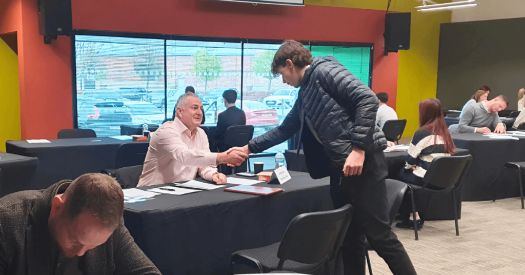 two people shaking hands at a table in front of a large window