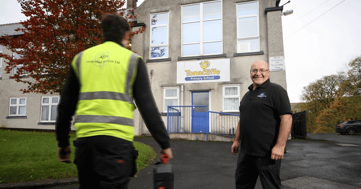 Image shows Sean Jackson stood smiling in front of Tonacliffe Primary School