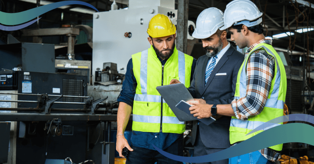 Image shows three mechanical and electrical engineers huddled together looking at a tablet. All wearing high vis vests and hard hats