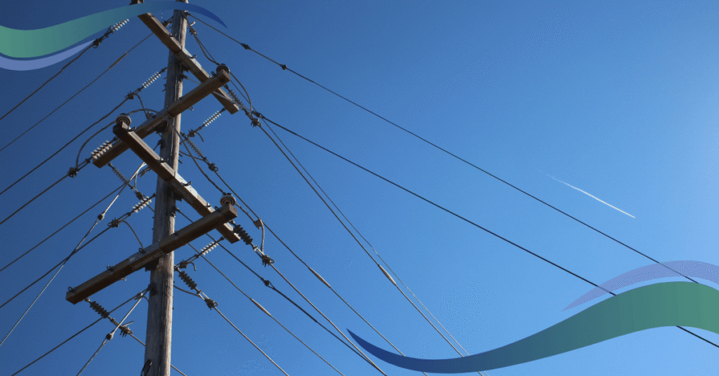 A utility pole with many wires against a clear blue sky with a distant airplane contrail.