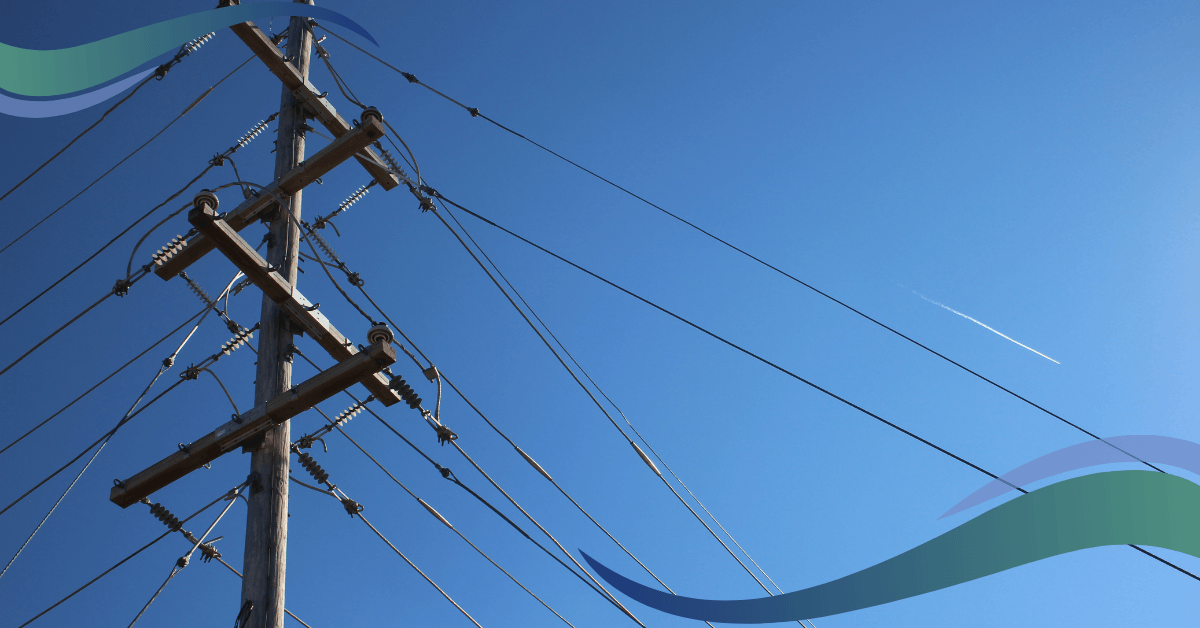 A utility pole with many wires against a clear blue sky with a distant airplane contrail.